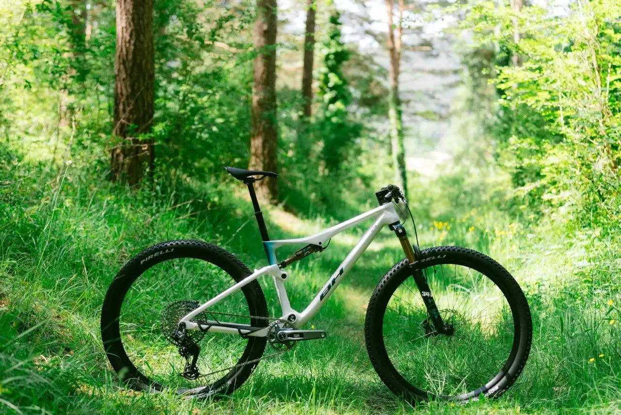 Bicicleta de montaña de suspensión total blanca con neumáticos negros y horquilla delantera de color dorado, con un diseño de cuadro elegante.
