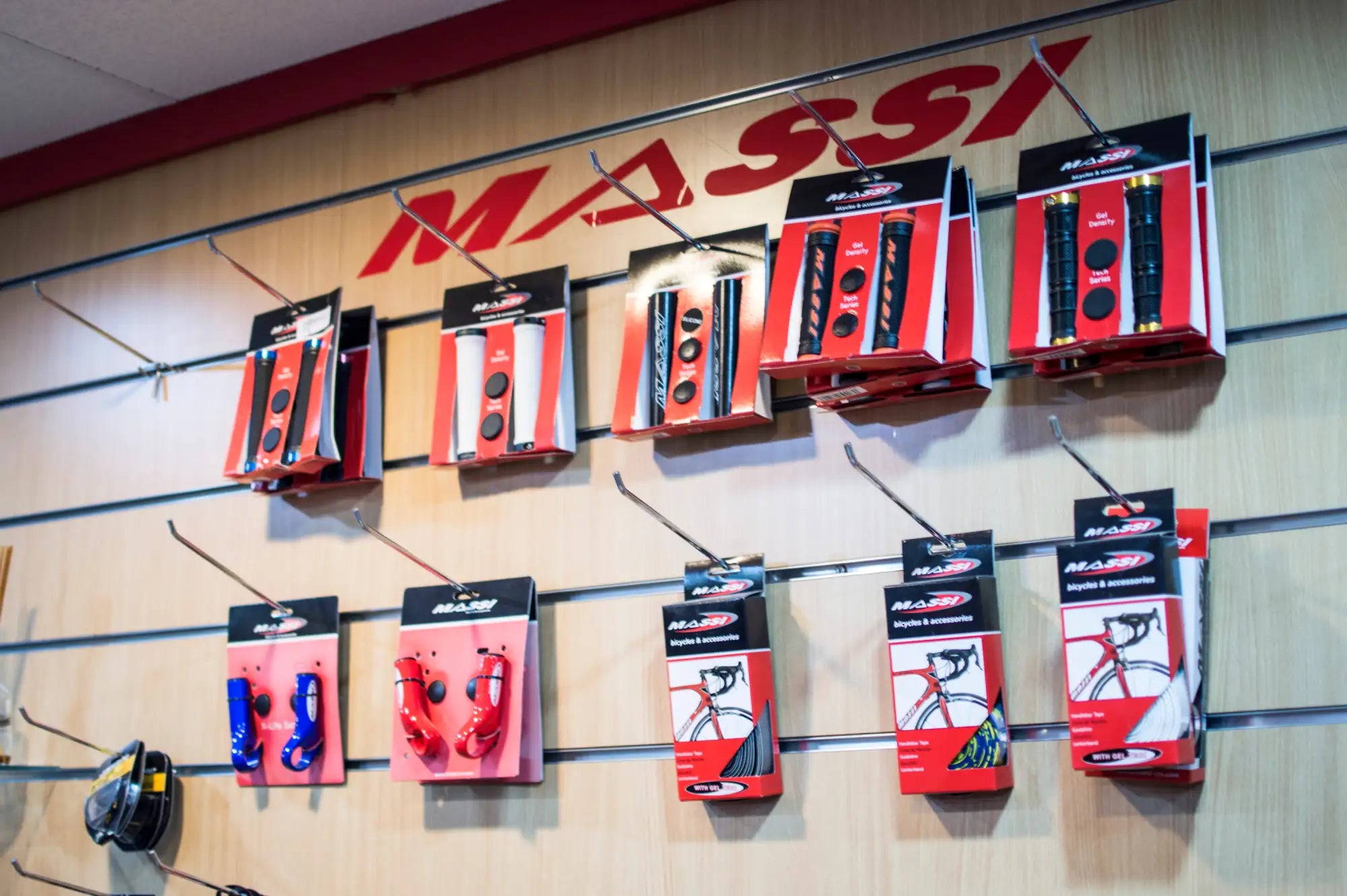 Paquetes de cinta para manillar de bicicleta Massi roja y negra exhibidos en un perchero de pared.