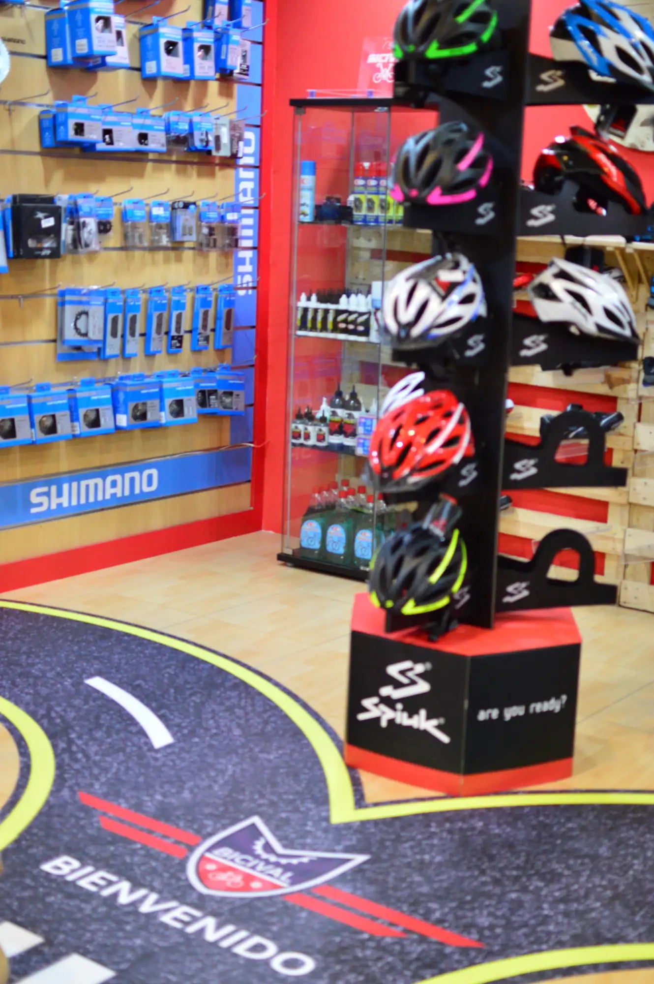 Un soporte de exhibición para cascos de bicicleta spiluk en negro y rojo que presenta múltiples cascos en varios colores como blanco, rosa, amarillo y verde.